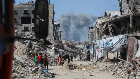 Asap mengepul ke arah utara menjadi latar ketika warga Palestina bergerak melalui Jabalia meninggalkan Jalur Gaza utara menuju Kota Gaza pada 19 Mei 2025. (Bashar TALEB/AFP)