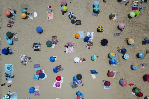 Foto udara menunjukkan orang-orang berjemur di pantai Costa da Caparica di Almada, dekat Lisbon, selama gelombang panas pertama tahun ini, pada tanggal 29 Juni 2025. (CARLOS COSTA/AFP)