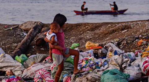 Seorang anak perempuan membawa adiknya berjalan di tumpukan sampah di permukiman kumuh di sepanjang garis pantai Pantai Baseco di Manila (28/9/2019). Daerah memiliki pantai yang sering