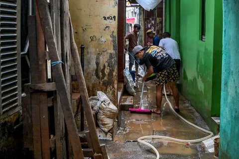 Warga membersihkan jalan di depan rumah mereka yang dipenuhi lumpur setelah banjir melanda lingkungan mereka setelah hujan deras di Jakarta pada Senin 7 Juli 2025. (BAY ISMOYO/AFP)