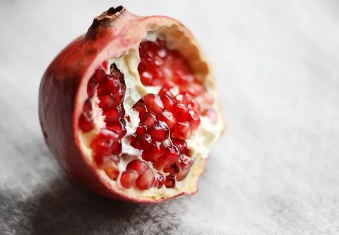 Buah delima utuh dan terbelah di atas sebuah piring kayu (Foto Dok: Freepik/azerbaijan_stockers).