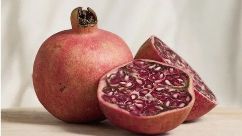 Buah delima utuh dan terbelah di atas sebuah piring kayu (Foto Dok: Freepik/azerbaijan_stockers).