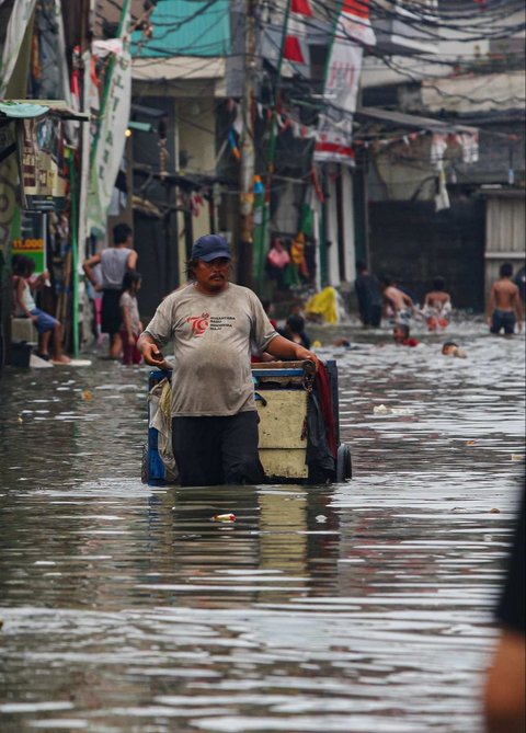 Warga melewati banjir rob yang merendam kawasan Muara Baru, Jakarta Utara, Selasa (14/1/2025).