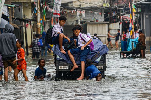 Sejumlah warga melewati banjir rob yang merendam kawasan Muara Baru, Jakarta Utara, Selasa (14/1/2025).