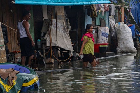 Warga melewati banjir rob yang merendam kawasan Muara Baru, Jakarta Utara, Selasa (14/1/2025).
