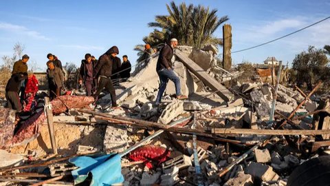 Orang-orang memeriksa sisa-sisa bangunan yang terkena serangan bom Israel di sebelah timur Khan Yunis, Jalur Gaza selatan pada 14 Januari 2025. (BASHAR TALEB/AFP)