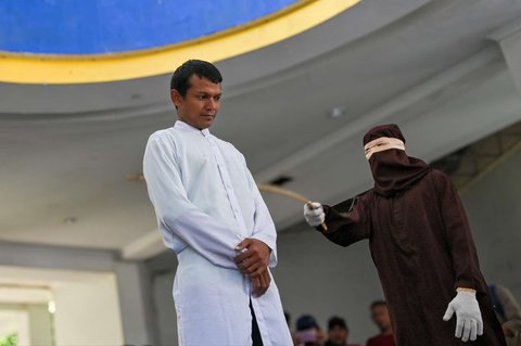 Ekspresi seorang pria tertunduk sambil menahan sakit ketika dicambuk berkali-kali oleh anggota polisi Syariah sebagai hukuman karena terbukti bermain judi online atau maisir di Banda Aceh, Aceh, pada 30 Januari 2025.