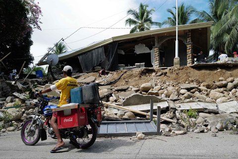 Seorang pengendara melewati sebuah rumah yang rusak akibat gempa bumi dahsyat di kota Manay, provinsi Davao Oriental, Filipina selatan, Sabtu, (11/10/2025).