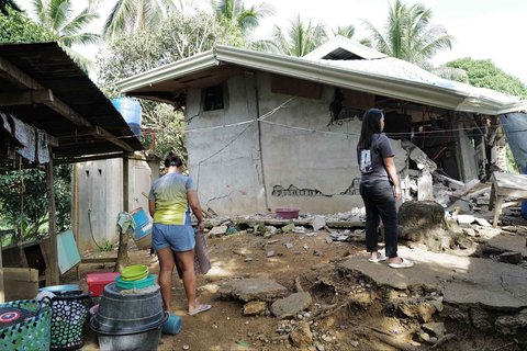 Warga berdiri di luar rumah yang rusak akibat gempa bumi dahsyat di kota Manay, provinsi Davao Oriental, Filipina selatan, Sabtu, (11/10/2025).