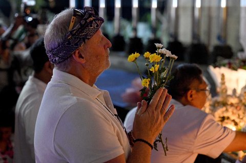 Seorang pria memegang bunga di tugu peringatan bagi mereka yang gugur dalam peringatan 23 tahun bom Bali 2002 di Kuta,  Bali, Indonesia, Minggu (12/10/2025).