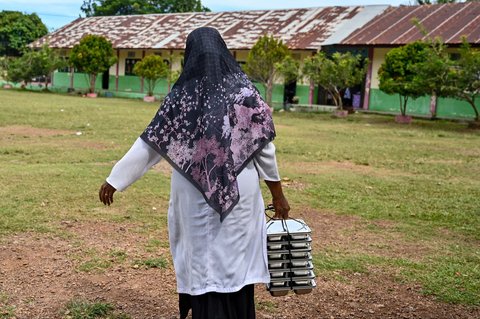 Seorang guru membawa nampan berisi makanan bergizi gratis ke ruang kelasnya di sebuah sekolah dasar di Darul Kamal, Aceh, Senin (13/10/2025).