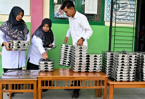 Guru membawa nampan berisi makanan bergizi gratis ke ruang kelasnya di sebuah sekolah dasar di Darul Kamal, Aceh, Senin (13/10/2025).