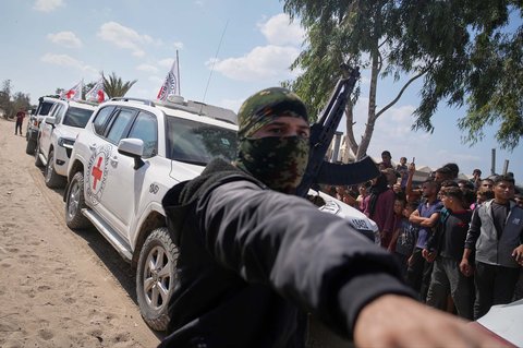 Kendaraan ICRC yang membawa sandera Israel yang dibebaskan melewati sekelompok warga Palestina dan kelompok bersenjata Hamas dalam perjalanan menuju perbatasan Israel, di Khan Younis, Jalur Gaza selatan, Senin (13/10/2025).