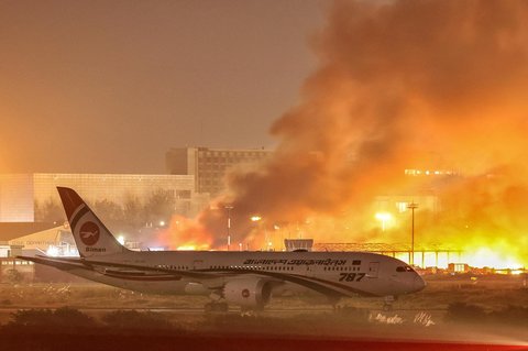 Sebuah pesawat berdiri di landasan sementara petugas pemadam kebakaran berusaha memadamkan kebakaran yang terjadi di bagian kargo Bandara Internasional Hazrat Shahjalal di Dhaka, Sabtu (18/10/2025) malam.