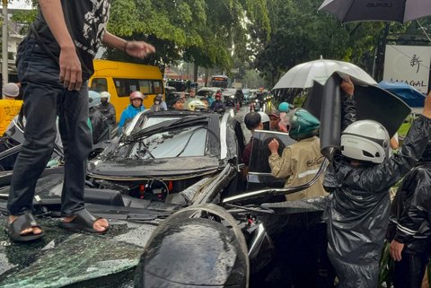 Warga mengevakuasi supir mobil mewah Lexus  yang tertimpa pohon tumbang di Jalan Metro Pondok Indah, Jakarta, Minggu (26/10/2025).
