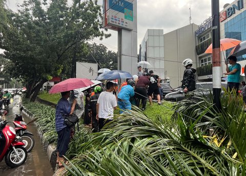 Warga mengevakuasi supir mobil mewah Lexus  yang tertimpa pohon tumbang di Jalan Metro Pondok Indah, Jakarta, Minggu (26/10/2025).