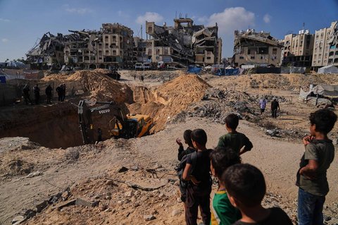 Anak-anak menyaksikan saat bekho dan dan pekerja  asal Mesir mencari jenazah para sandera di dekat kamp tenda pengungsi Palestina di Kota Hamad, Khan Younis, di Jalur Gaza selatan, Selasa, (28/10/2025).