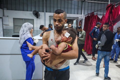 Seorang pria membawa seorang anak yang terluka akibat serangan Israel ke rumah sakit Al-Awda di Nuseirat, Jalur Gaza tengah, Rabu (29/10/2025).