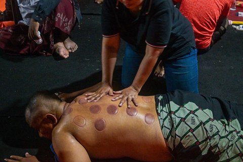Seorang pria dipijat  usai menjalani terapi bekam menggunakan tanduk sapi, yang disediakan oleh para relawan di tenda sementara yang didirikan untuk menampung keluarga santri yang hilang di Rumah Sakit Bhayangkara, Surabaya, Minggu (05/10/2025) malam.