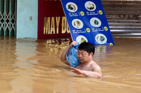 Seorang pria membawa botol air berjalan melewati banjir setelah hujan deras akibat Topan Matmo di kota Thai Nguyen, Vietnam, Rabu (08/10/2025).