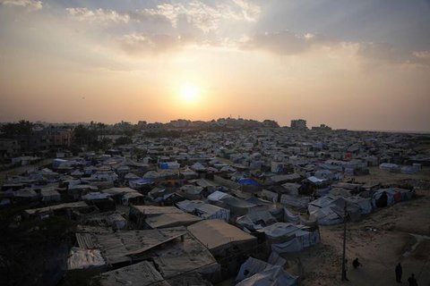 Seorang anak laki-laki Palestina yang sedang bermain membawa sepanci makanan yang ia terima dari sebuah tempat penampungan tempat tinggal keluarga-keluarga di Nuseirat, pusat Jalur Gaza, pada