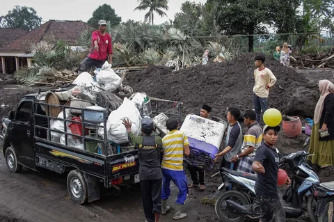 Warga menyelamatkan barang-barang dari sebuah rumah yang hancur akibat aliran piroklastik Gunung Semeru di Desa Supiturang, Lumajang, Jawa Timur, Jumat (21/11/2025).