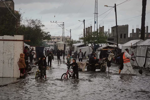 Warga Palestina berjalan di jalanan yang terendam banjir di samping kamp tenda sementara setelah hujan deras di Deir al-Balah, Jalur Gaza tengah, Selasa (25/11/2025).