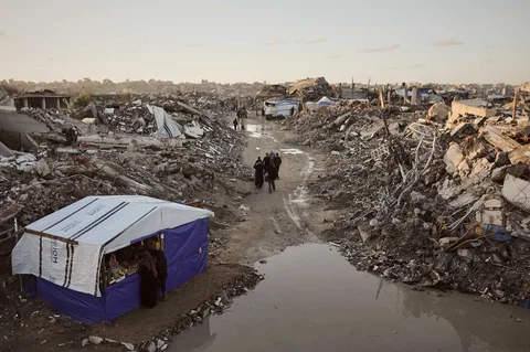 Warga Palestina berjalan diantara reruntuhan bangunan yang hancur dengan kondisi banjir Sebagian  di utara Kota Gaza, Selasa, (25/11/2025).