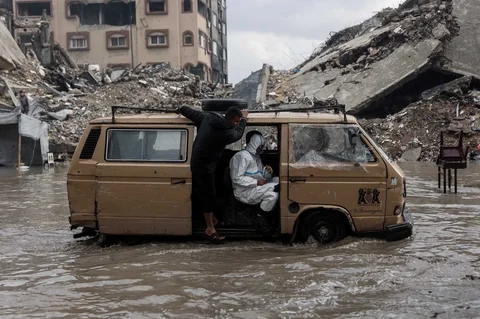 Warga menaiki kendaraan  menerobos banjir di kamp darurat yang menampung warga Palestina yang terlantar di Kota Gaza, Selasa, (25/11/2025).