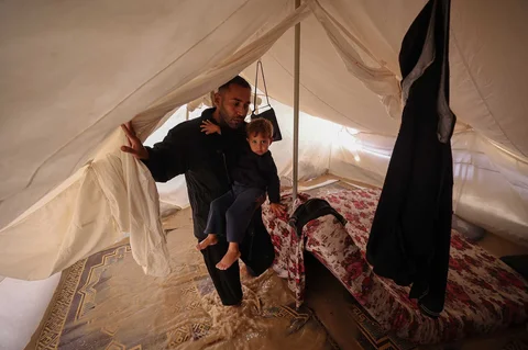 Warga menggendong anaknya di dalam tenda yang banjir  kamp pengungsi Maghazi di Jalur Gaza tengah, Selasa, (25/11/2025).