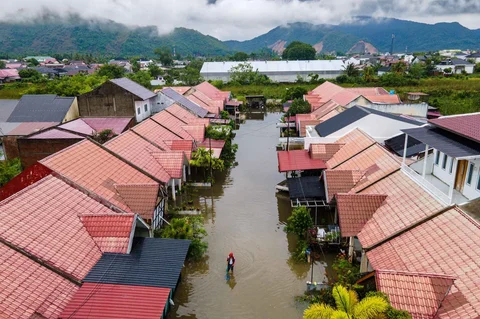 Foto udara menunjukkan seorang pria mengarungi banjir setelah hujan deras di permukiman Darul Imarah di pinggiran Banda Aceh, Kamis (27/11/2025).