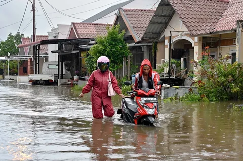 Warga mendorong sepeda motornya menerobos banjir di jalan yang tergenang setelah hujan deras di permukiman Darul Imarah, pinggiran Banda Aceh, Kamis (27/11/2025).