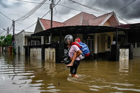 Warga melewati banjir di jalan yang tergenang setelah hujan deras di permukiman Darul Imarah, pinggiran Banda Aceh, Kamis (27/11/2025).