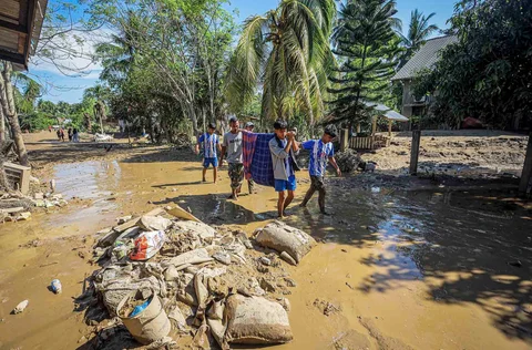 Warga  menggotong  seseorang yang sakit  saat berjalan melewati puing-puing banjir  di Bireuen, Provinsi Aceh, Sabtu (29/11/2025).