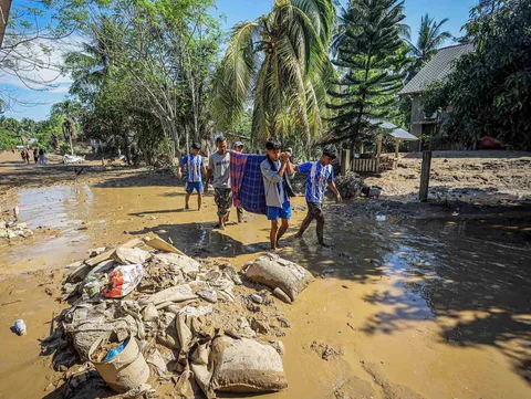 Warga menggotong seseorang yang sakit saat berjalan melewati puing-puing banjir di Bireuen, Provinsi Aceh, Sabtu (29/11/2025).