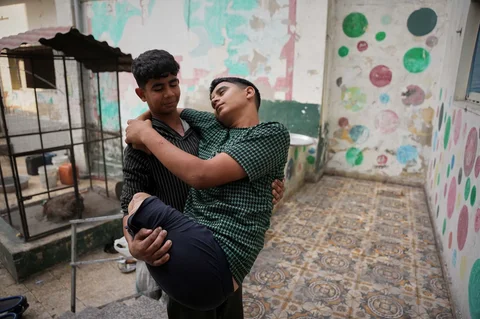 Mohammed Al-Samri (14) menggendong kakaknya, Youssef (16), yang kehilangan kedua kakinya akibat serangan udara Israel pada Mei lalu, di taman kanak-kanak yang menjadi tempat pengungsian mereka di kawasan Al-Tuffah, Kota Gaza, Senin (24/11/2025).