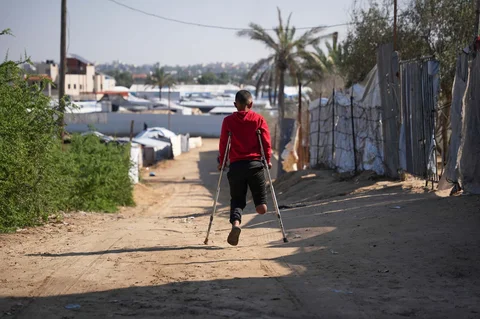 Fadi al-Balbisi (12) berjalan menggunakan kruk sepulang dari pelatihan rehabilitasi kaki palsu di Rumah Sakit Hamad, Zawaida, Jalur Gaza tengah, Kamis (4/12/2025), setelah kaki kanannya diamputasi akibat tembakan artileri tentara Israel pada 28 April lalu.