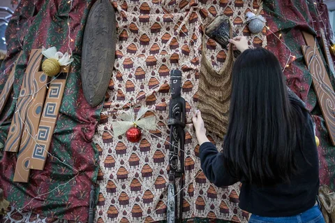 Mahasiswa Indonesia berdiri di samping dekorasi Natal sepanjang 63 meter bermotif budaya Papua yang dibuat dengan bantuan AI dan dihiasi Tifa, perisai Asmat, serta ornamen tradisional di Universitas Petra Surabaya, Kamis (18/12/2025).