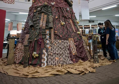 Mahasiswa Indonesia berpose di samping dekorasi Natal sepanjang 63 meter bermotif budaya Papua yang dibuat dengan bantuan AI dan dihiasi Tifa, perisai Asmat, serta ornamen tradisional di Universitas Petra Surabaya, Kamis (18/12/2025).