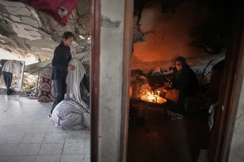 Amani Halawa menyalakan api sementara putrinya, Aya, mengatur cucian di rumah mereka yang rusak di Kota Gaza, Selasa (25/11/2025).