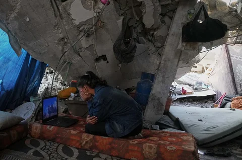 Bisan Taroush menonton film di laptop di bawah atap rumahnya yang sebagian runtuh di Kota Gaza, Selasa, (11/11/2025).