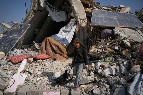Rita Abu Shaqfa bermain dengan anjingnya di depan rumah mereka yang runtuh di Kota Gaza, Jumat (21/11/2025).