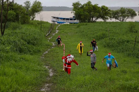 Relawan Jorge Alberto Barrozo, yang mengenakan kostum Sinterklas, mengantarkan hadiah kepada anak-anak di komunitas tepi sungai di daerah pedesaan Careiro da Varzea, negara bagian Amazonas, Brasil, Sabtu (20/12/2025) waktu setempat.