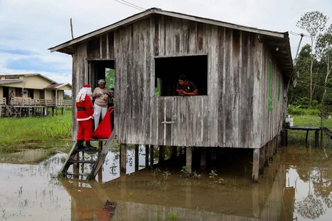 Relawan Jorge Alberto Barrozo, yang mengenakan kostum Sinterklas, mengantarkan hadiah kepada anak-anak di komunitas tepi sungai di daerah pedesaan Careiro da Varzea, negara bagian Amazonas, Brasil, Sabtu (20/12/2025) waktu setempat.