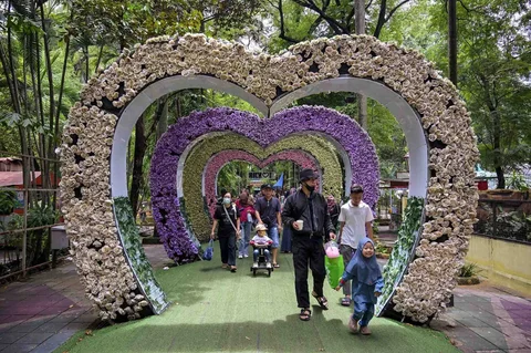 Pengunjung berjalan melewati dekorasi berbentuk hati di Kebun Binatang Surabaya selama liburan Natal dan Tahun Baru di Surabaya, Minggu (21/12/2025).