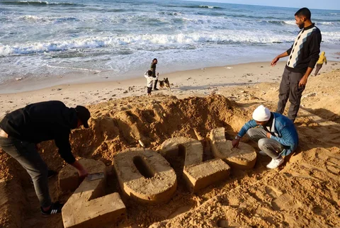 Seniman Yazed Abo Jarad (kiri) membuat patung pasir untuk tahun 2026  saat pengungsi Palestina bersiap menyambut Tahun Baru di Deir El-Balah di Jalur Gaza tengah, Selasa (30/12/2025).