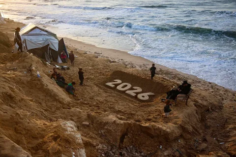 Anak-anak berdiri di samping patung pasir saat pengungsi Palestina bersiap menyambut Tahun Baru di Deir El-Balah di Jalur Gaza tengah, Selasa (30/12/2025).