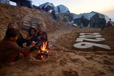Anak-anak berdiri di samping patung pasir saat pengungsi Palestina bersiap menyambut Tahun Baru di Deir El-Balah di Jalur Gaza tengah, Selasa (30/12/2025).