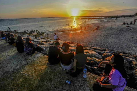 Wisatawan  duduk pada beton abrasi pantai mennyaksikan suasana senja  di Pantai Kelan, Badung, Bali.