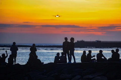 Wisatawan  duduk pada beton abrasi pantai mennyaksikan suasana senja  di Pantai Kelan, Badung, Bali.